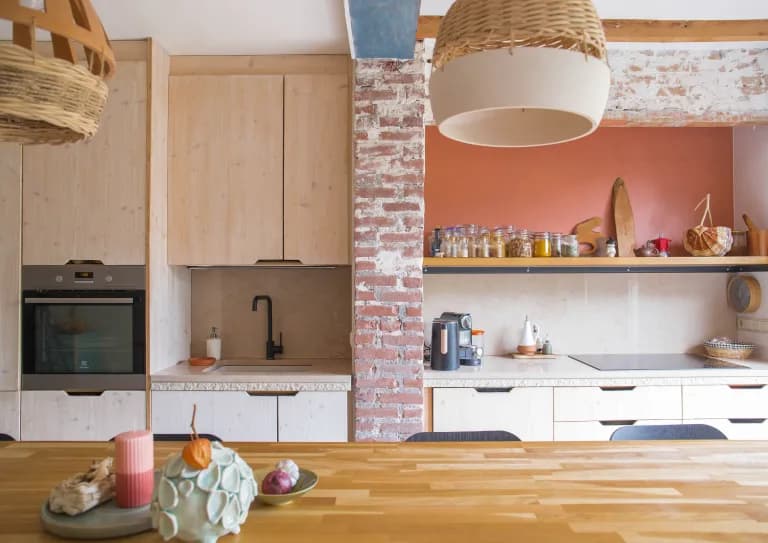 A handcrafted kitchen with pale wood cabinetry, an exposed brick pillar and a terracotta wall
