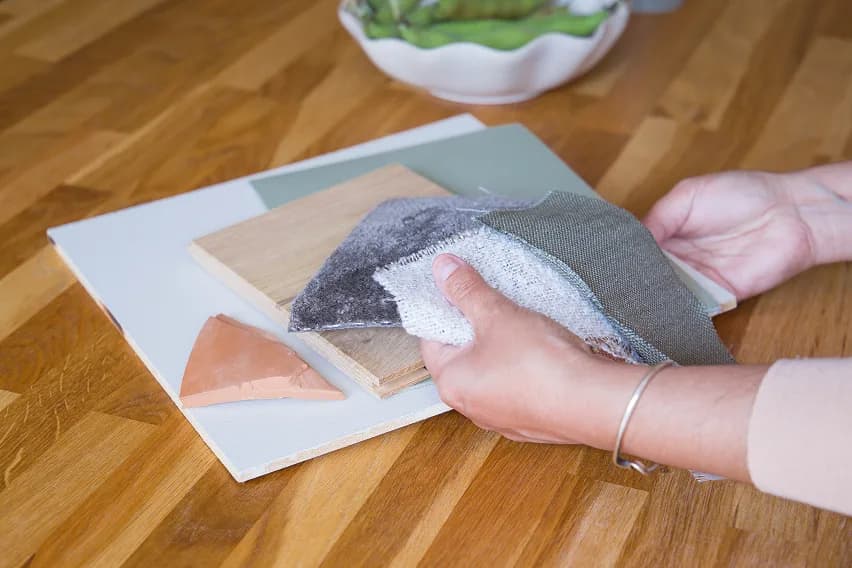 Hands laying out wood, fabric and terracotta material swatches on a wooden floor