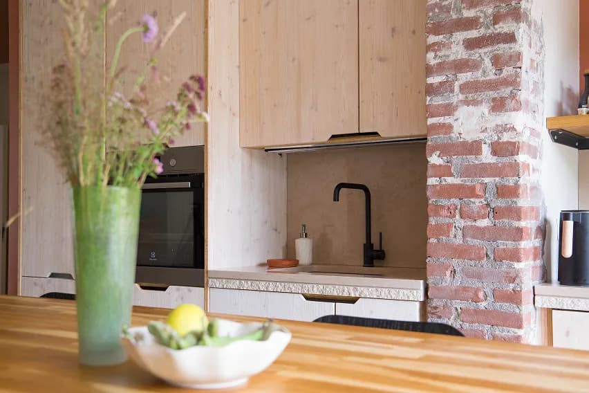 Kitchen with pale wood cabinetry, a black tap and an exposed brick pillar