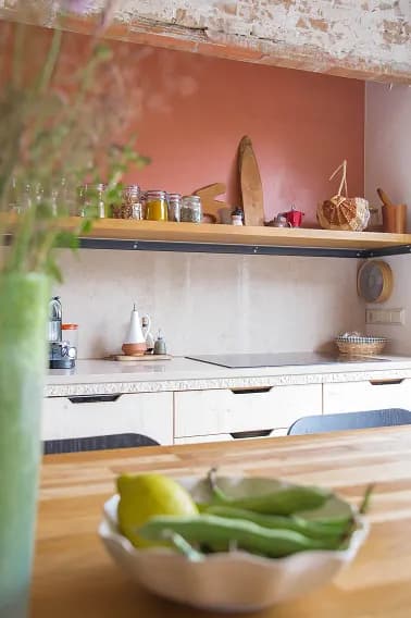 Kitchen corner with a terracotta wall, open shelving, glass jars and woven baskets