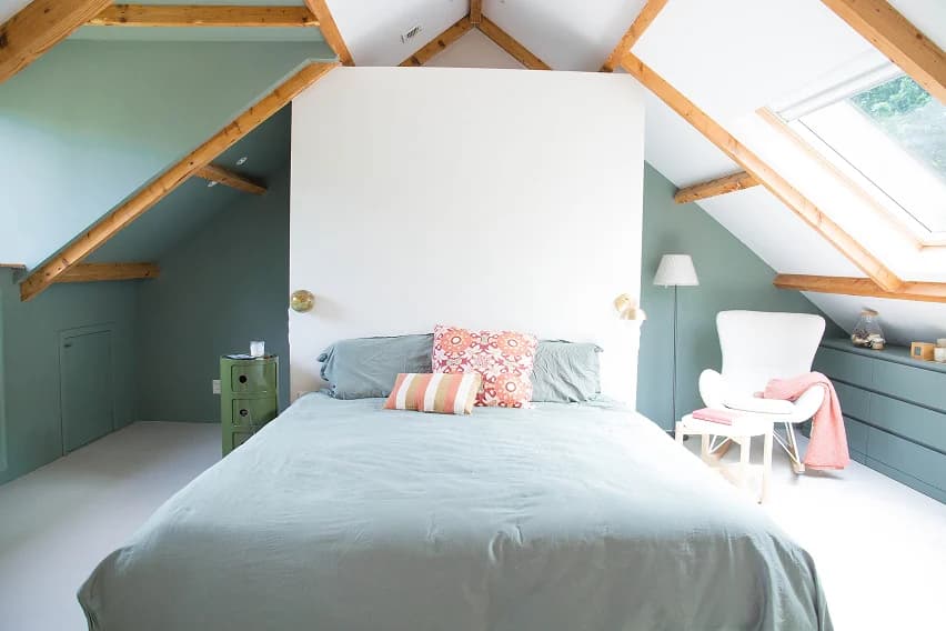 Attic bedroom with sage green walls, exposed timber beams and a skylight above the bed