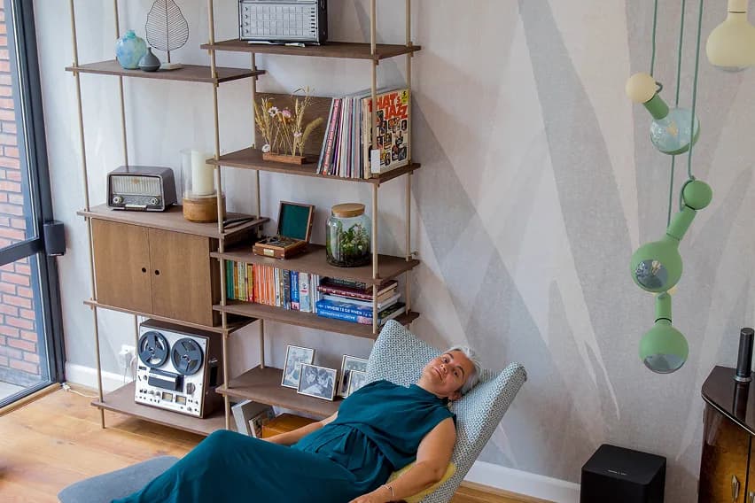 A woman reclining beside open shelving filled with books, records and vintage electronics