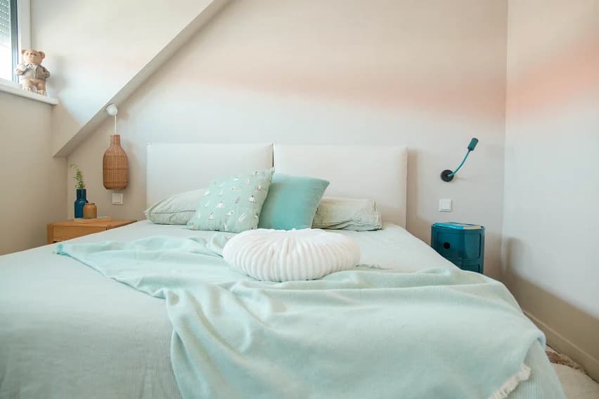 Pale blue-green bedroom with layered linen bedding and a soft knit cushion
