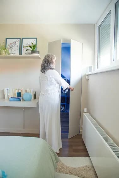 A woman opening a built-in wardrobe in a white bedroom with a blue accent nook