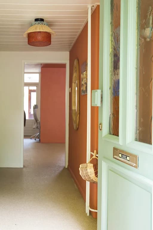 A hallway with a terracotta wall and an open mint-green front door, leading into a warmly lit home